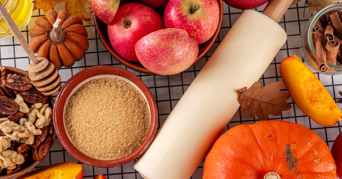 a cluttered counter with apples, cinnamon, pumpkin, shelled walnuts, a rolling Pin and a bowl of natural sugar. Festive fall.